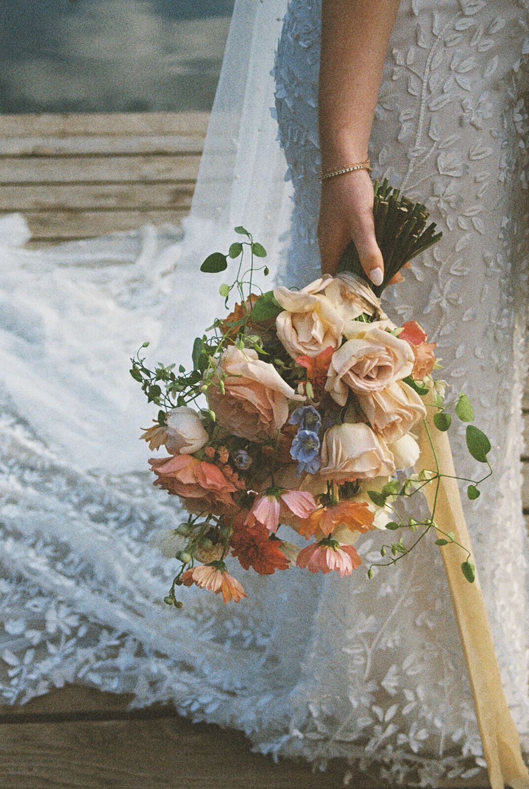 A bride's hand holding a flower bouquet down by her side.