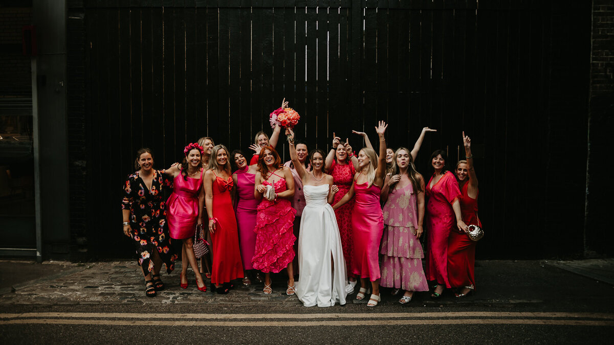 A bride and her bridesmaids who are all wearing pink party in front of a black gate at Shoreditch Studios. 