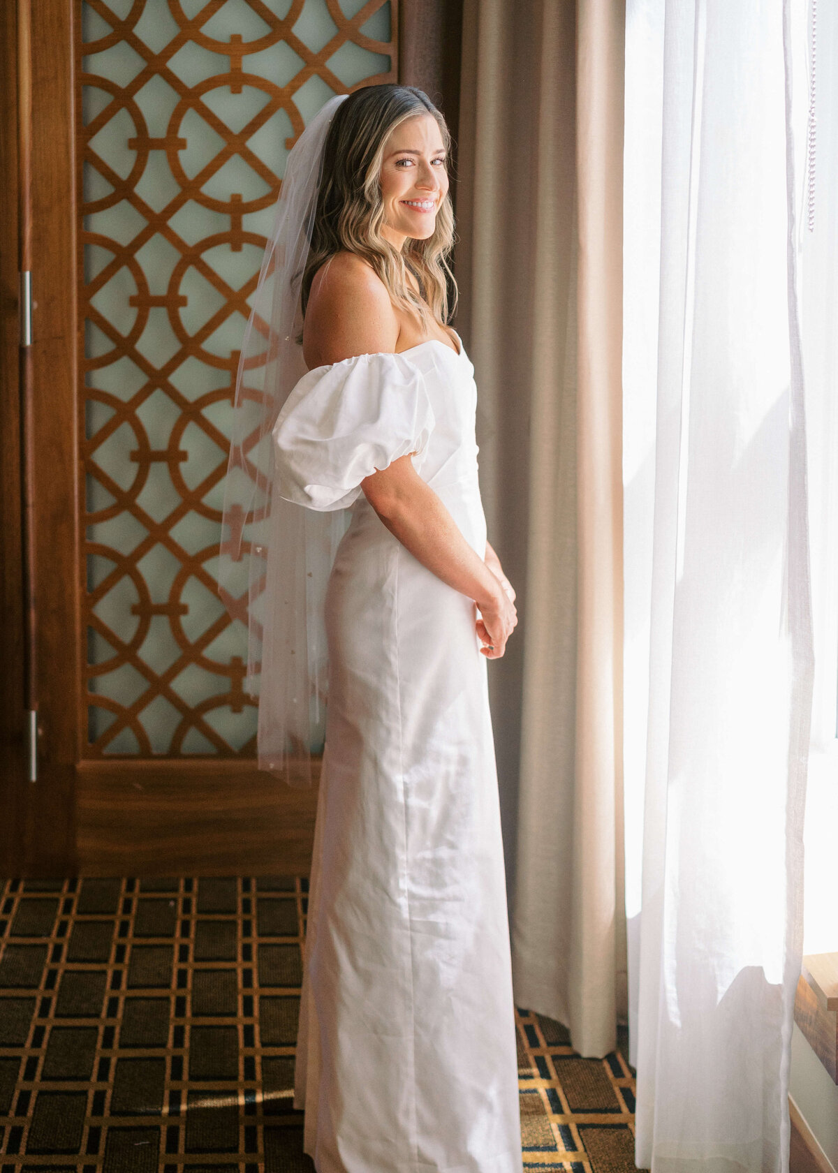 Elegant bride in front of the hotel window and smiling at the camera