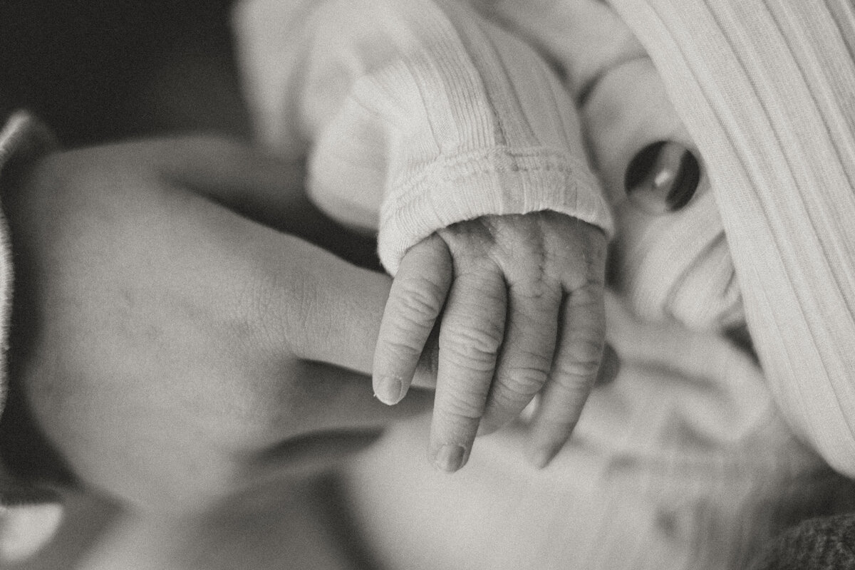 mom holding newborn baby's hand in black and white in Firestone Colorado