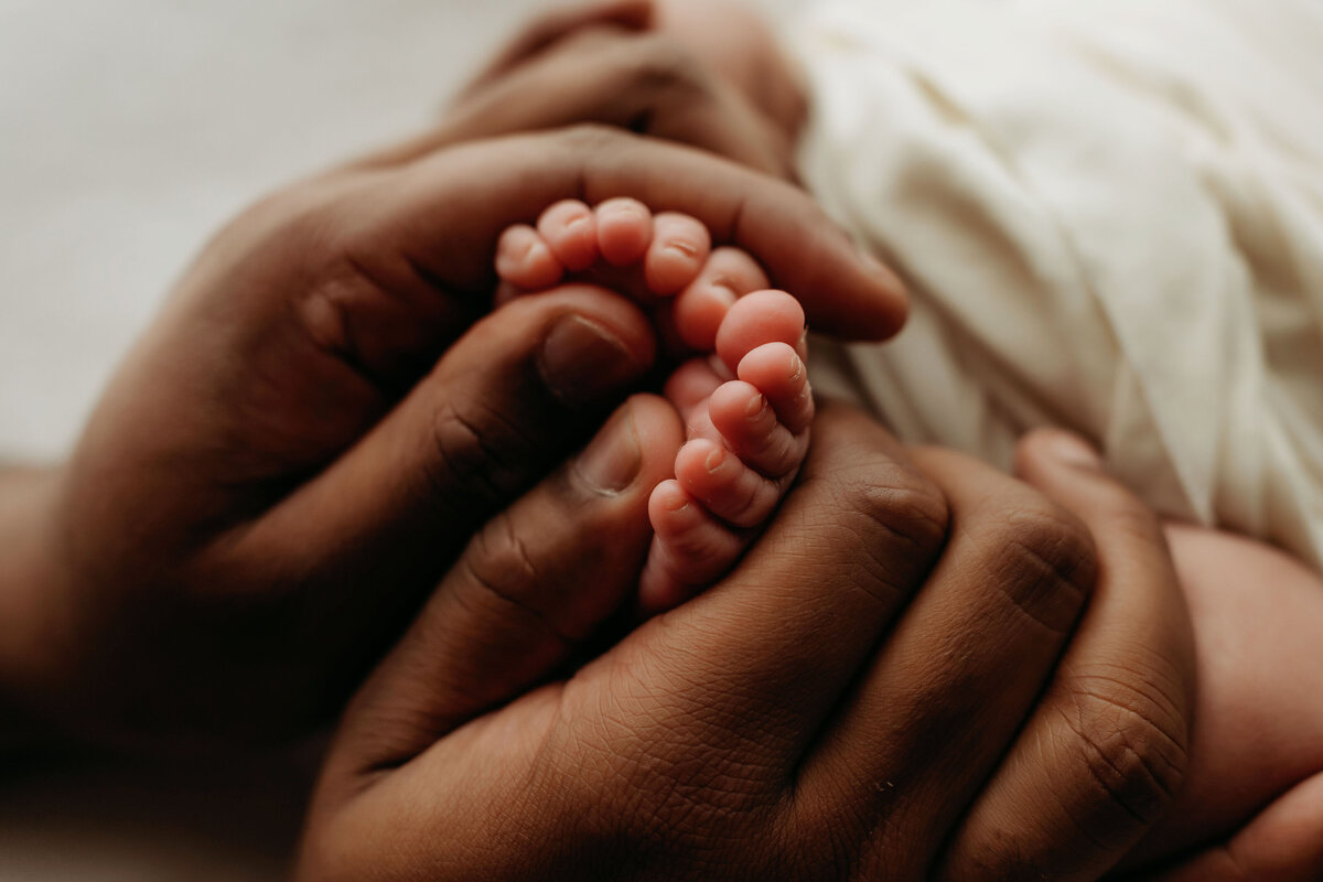 A dad holds his newborn's tiny feet in his hands, bathed in natural light inside a Vancouver, Washington studio