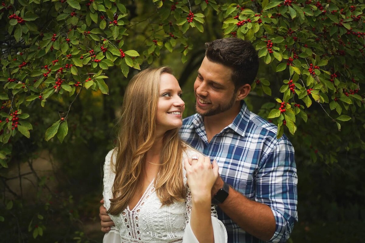 A couple standing closely in a lush green setting with red berries in the foreground