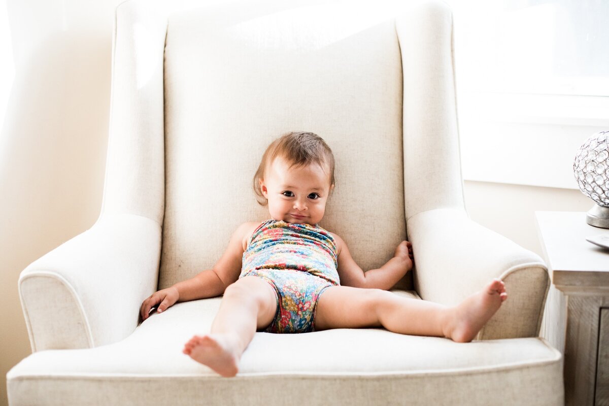A toddler lounging casually on a white armchair with a curious expression, captured elegantly by a Pittsburgh family photographer.
