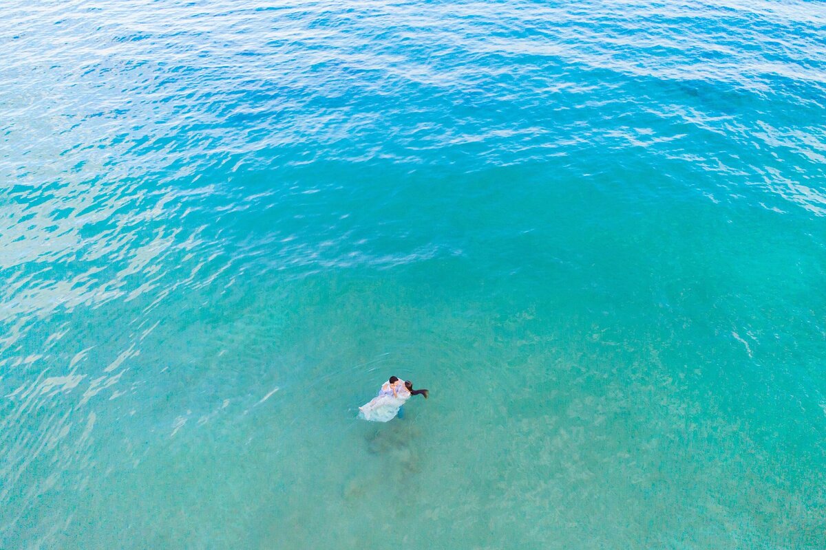 Woman and man embrace in turquoise waters during their drone couples portraits in Maui