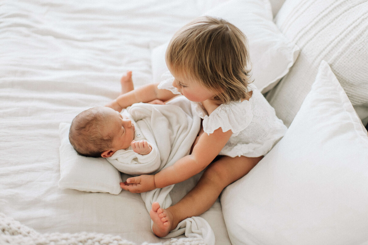 toddler big sister sitting with newborn baby between her legs