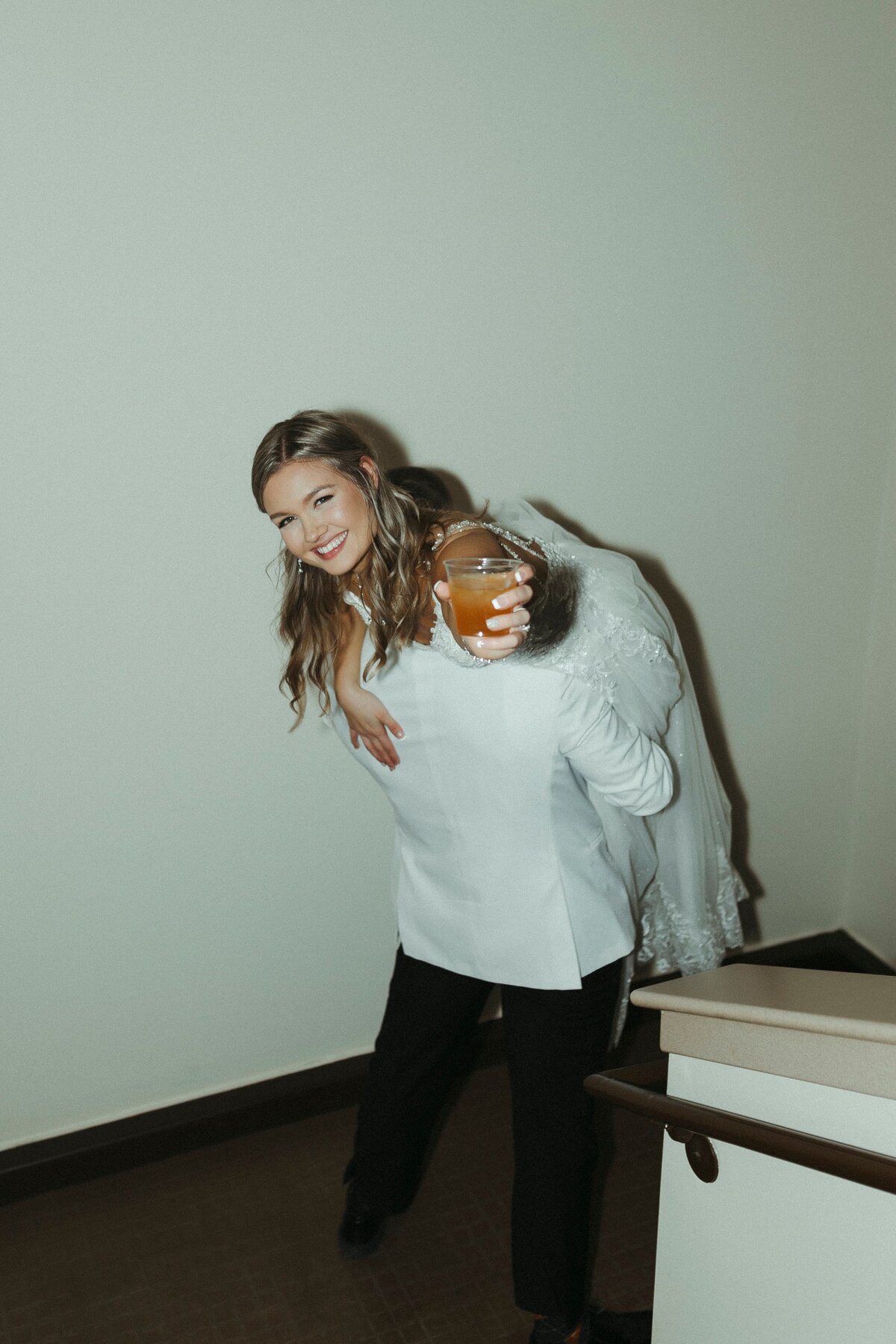 bride holding her drink while groom carries her away