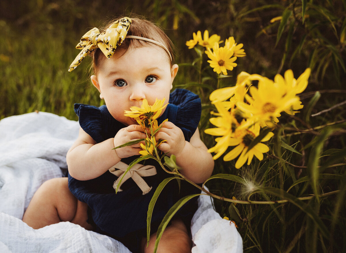 Baby girl mischievously smelling yellow wildflowers.
