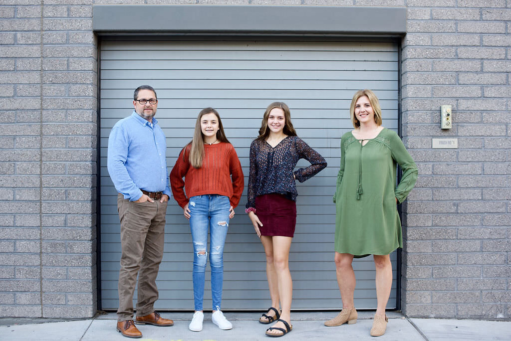 A small family smiling and standing in front of an industrial door.