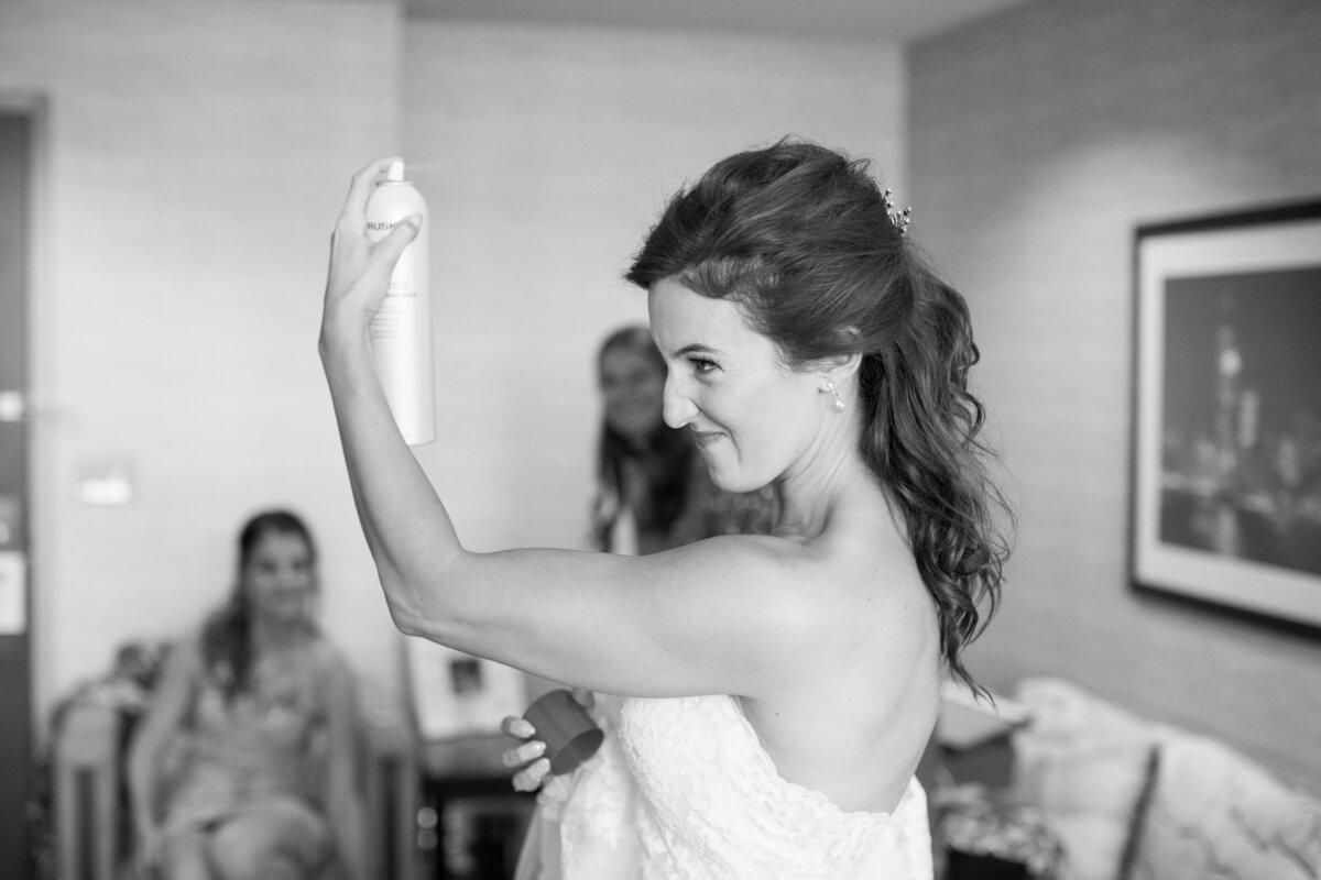 bride sprays her hair after getting into her gown