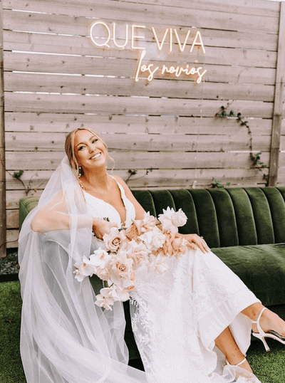 Bride sitting on a green velvet couch with soft glam bridal hair and makeup by professional San Antonio makeup artist, featuring full makeup services and radiant skin