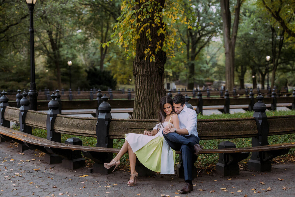 The happily engaged couple is sitting on the bench at Central Park, New York City during fall. Image by Jenny Fu Studio.