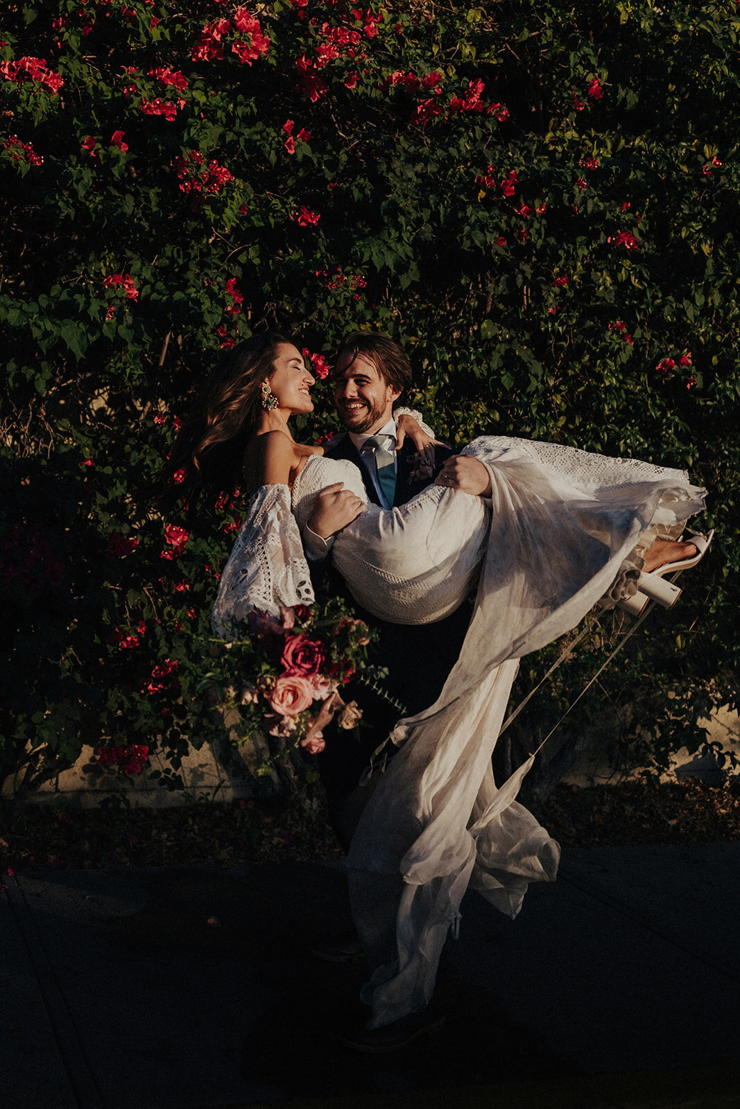 A handsome groom twirls his bride in front of a bougainvillea bush