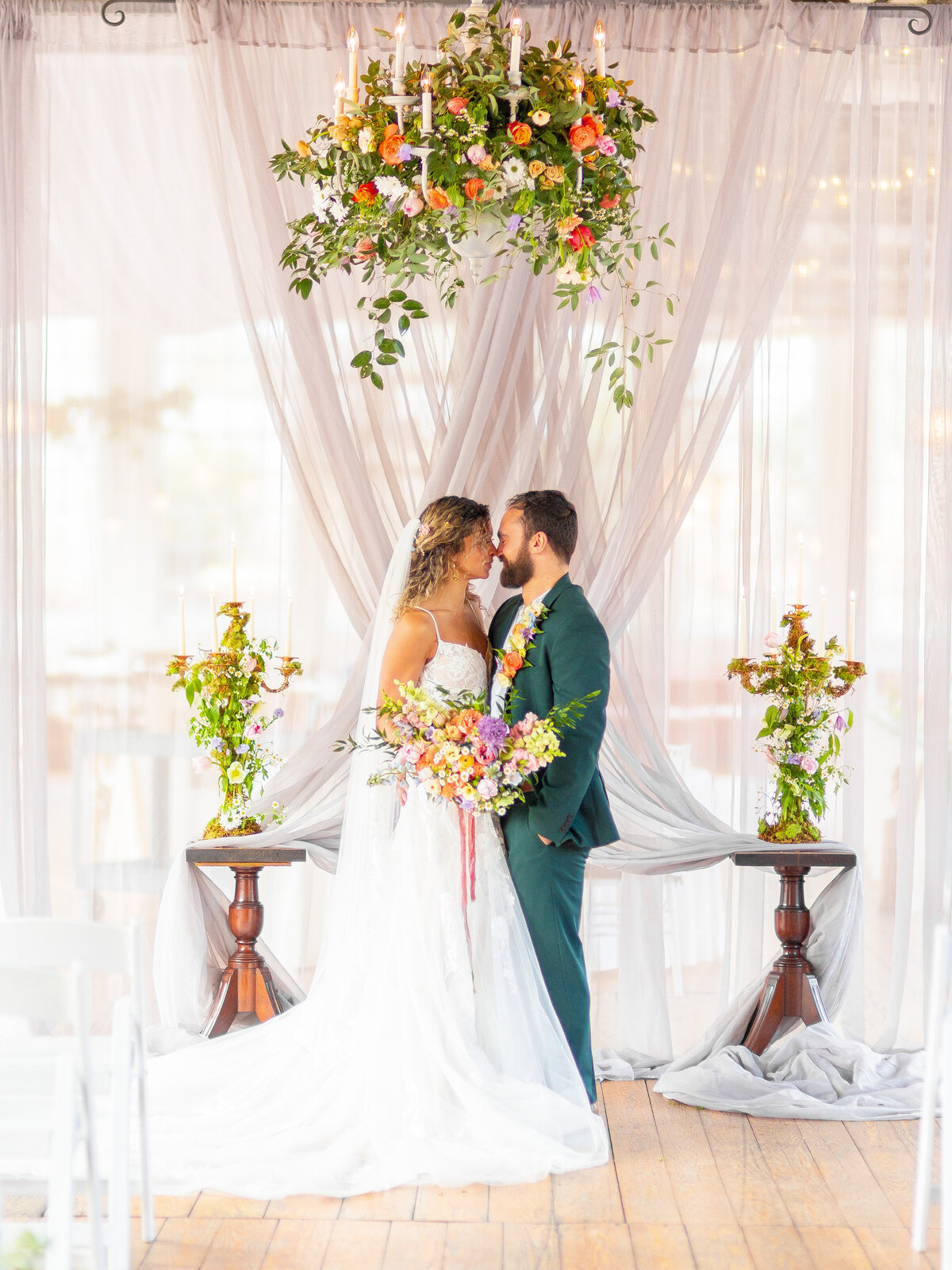 Bride and groom kissing at the alter with flower arrangement above their heads