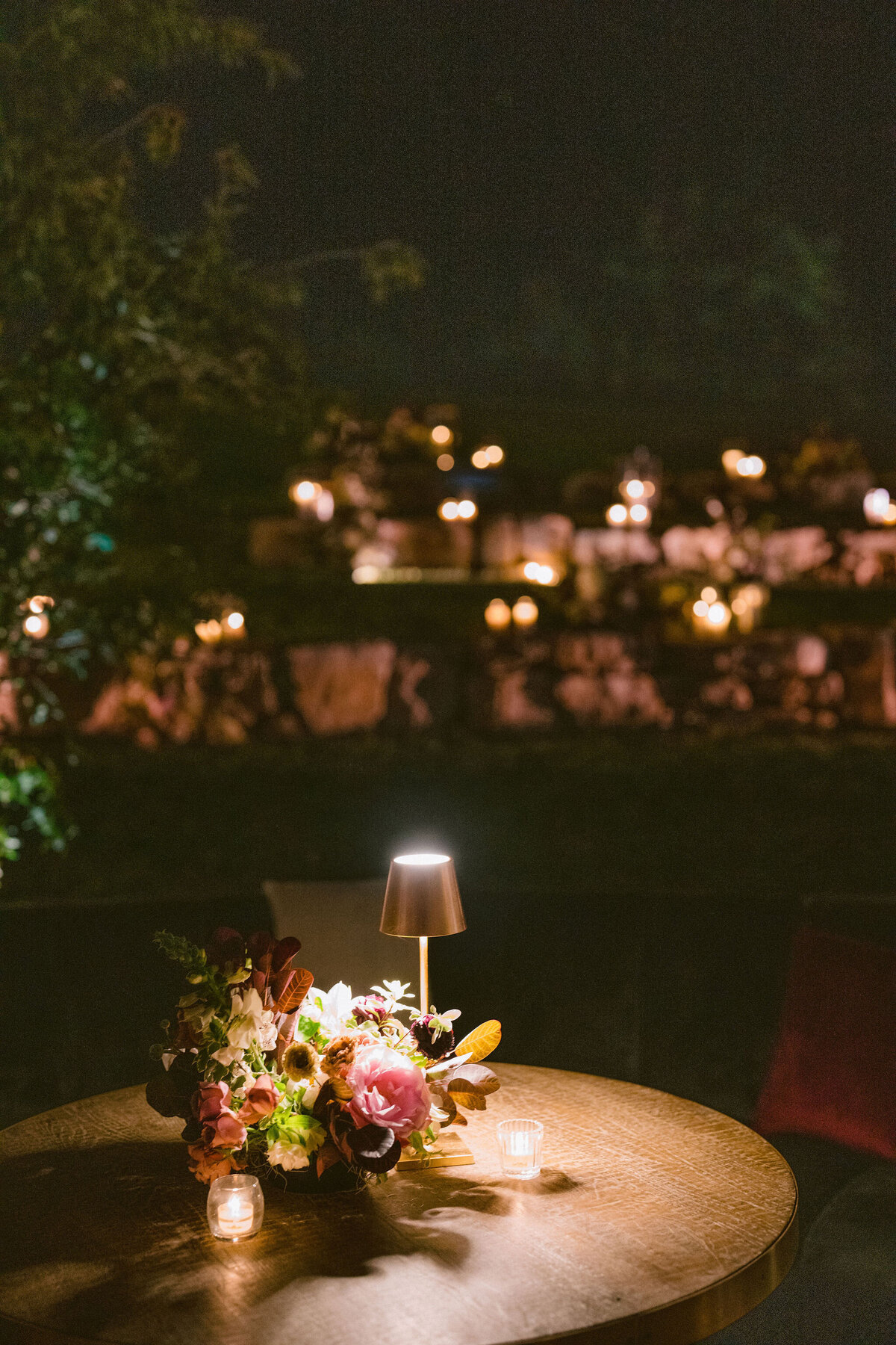 Moody welcome party for fall wedding weekend. Tented reception for outdoor wedding reception at Blackberry Farm. Moody floral design with colors of deep magenta, mauve, eggplant, blush, and natural greens. Rich tones with roses, mums, and smokebush foliage. Romantic candle light and large trees create a magical setting for a welcome party. Destination wedding at Blackberry Farm. Design by Rosemary & Finch Floral Design in Nashville, TN.