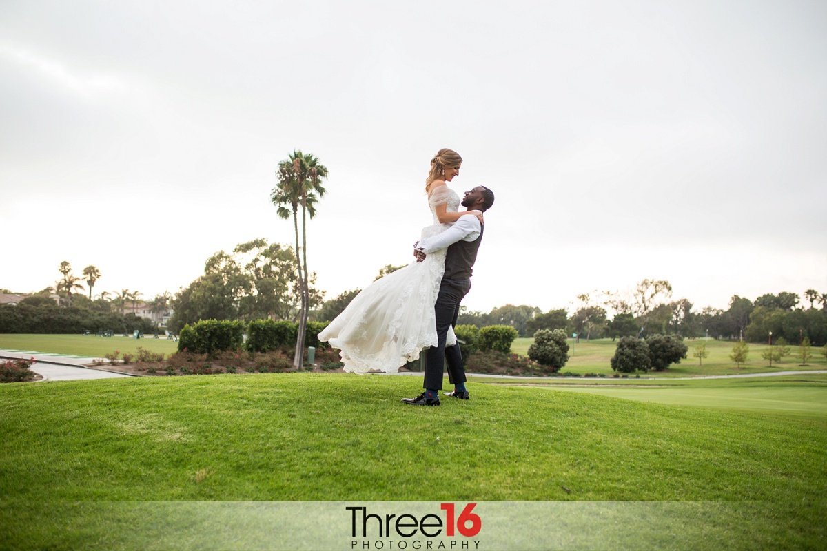Groom lifts his new Bride high in the air during a photo shoot on the golf course at the SeaCliff Country Club