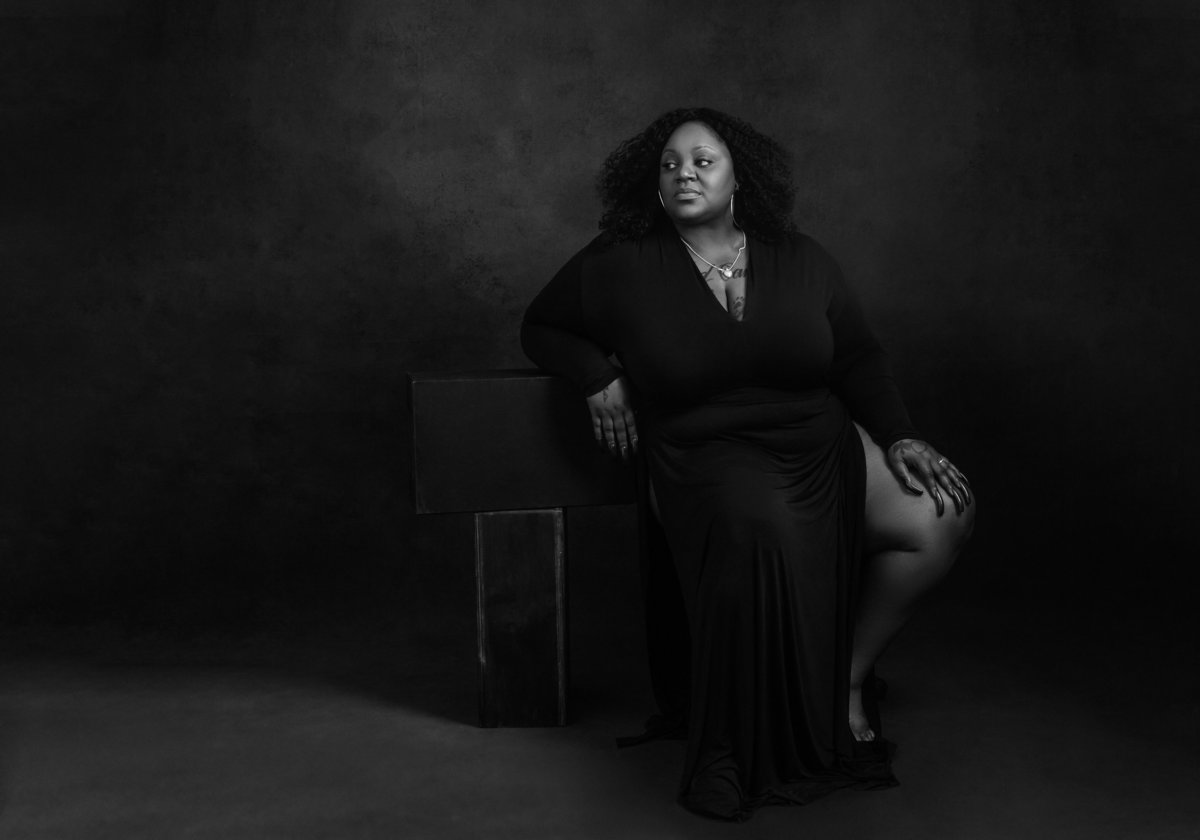 An African American black woman in a black dress reclines for a black and white picture at Janel Lee Photography studios in Cincinnati Ohio