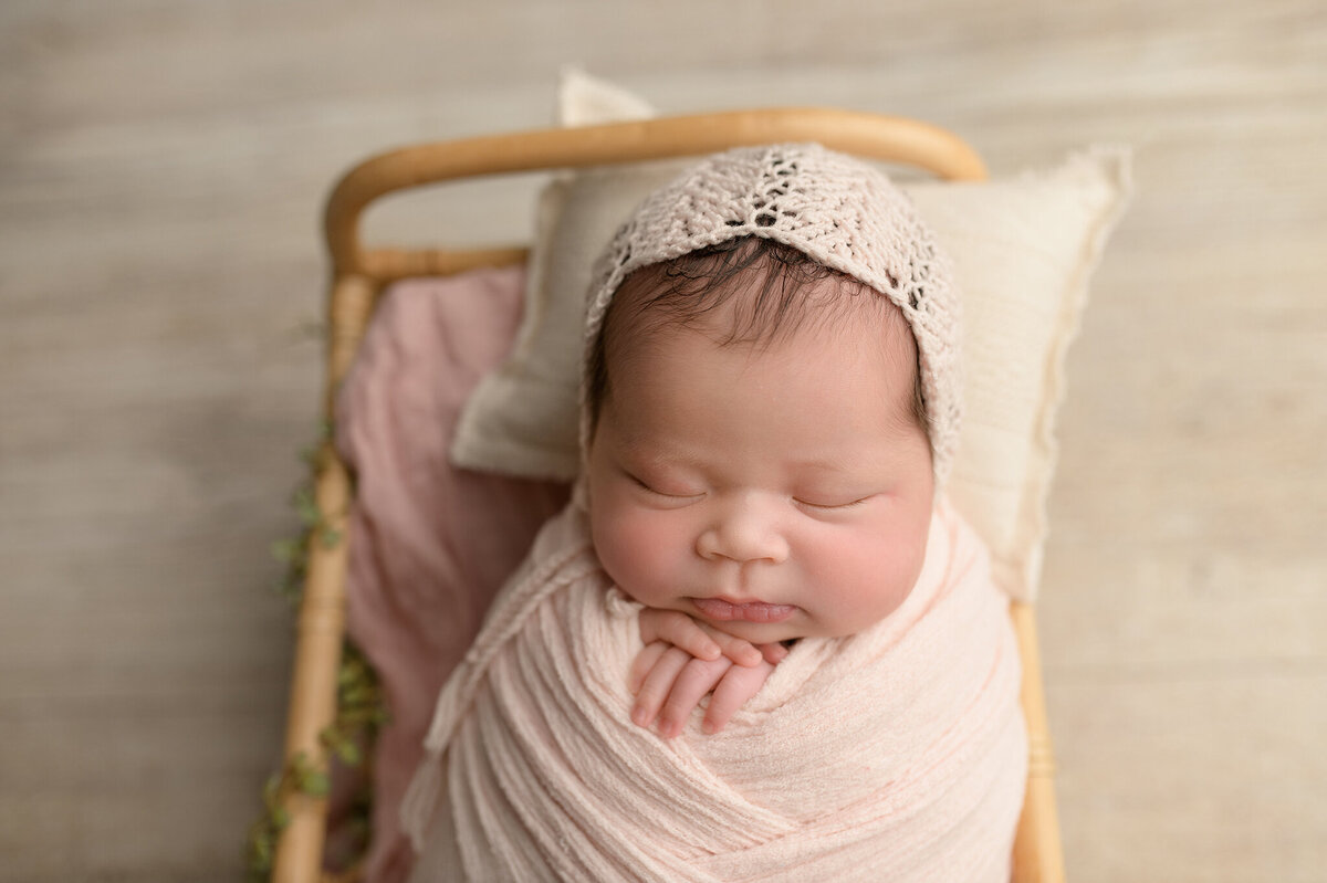 Newborn baby girl in pink swaddle wearing a bonnet