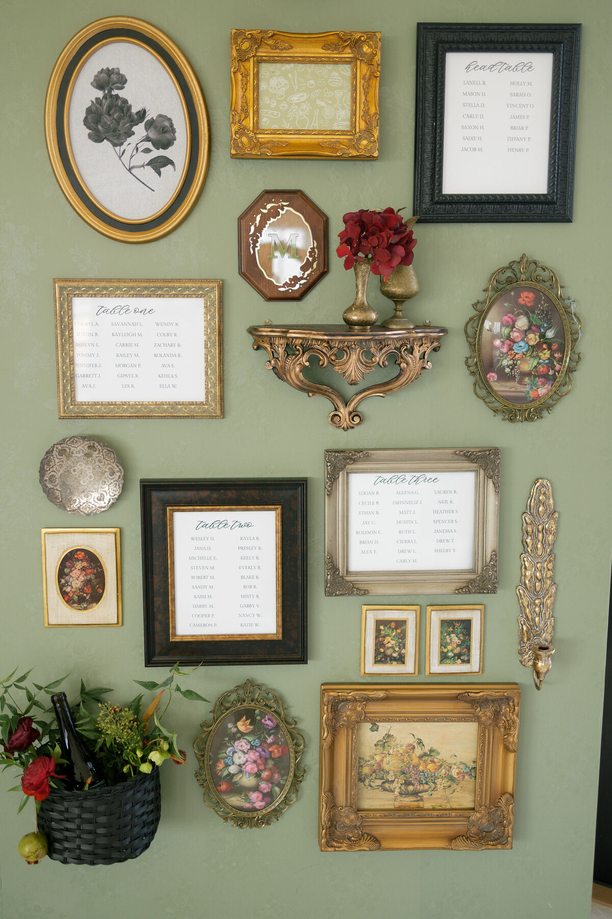 Vintage-inspired wedding seating chart displayed as an eclectic gallery wall of ornate gold, bronze, and black frames arranged on a sage green textured backdrop, blending florals, art, and guest lists for a unique reception design.