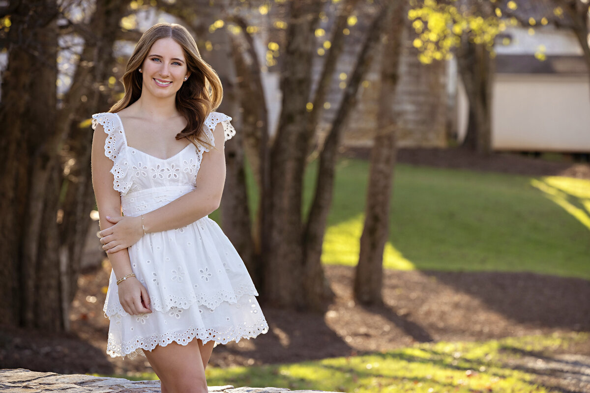 High school senior in white dress with rich fall leaves and soft golden hour glow near Charlotte NC