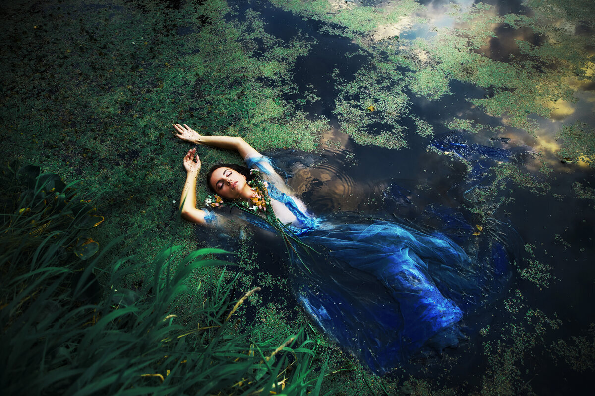 Femme en longue robe bleue étendue dans une eau bleue nuit et algues vertes.