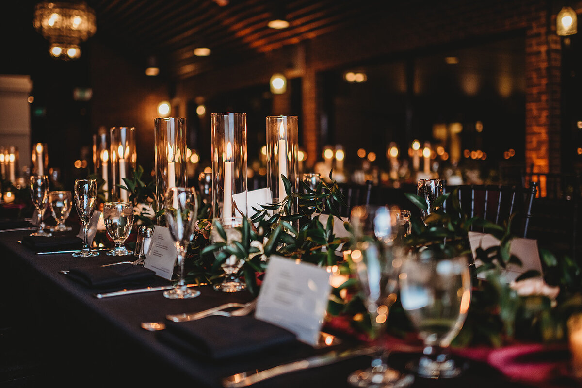 Indoor wedding decorations for reception captured by Maryland wedding photographer with tall candles on every table and dark linens as well as greenery for Baltimore wedding