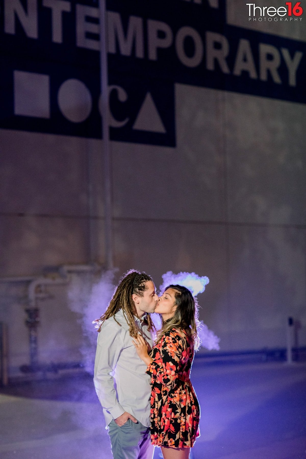 Engaged couple share a tender kiss with smoke behind them