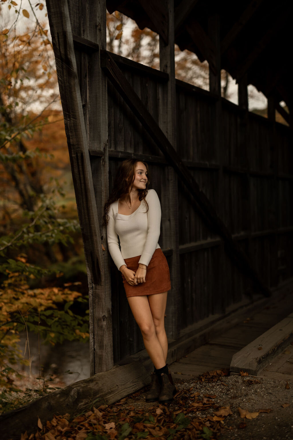 A person wearing a sleeveless top smiles while holding a blue mug, captured beautifully in this portrait photography. They are seated indoors with a blurred couch and pillow visible in the background, as sunlight casts soft shadows across the scene, evoking a cozy New England vibe.