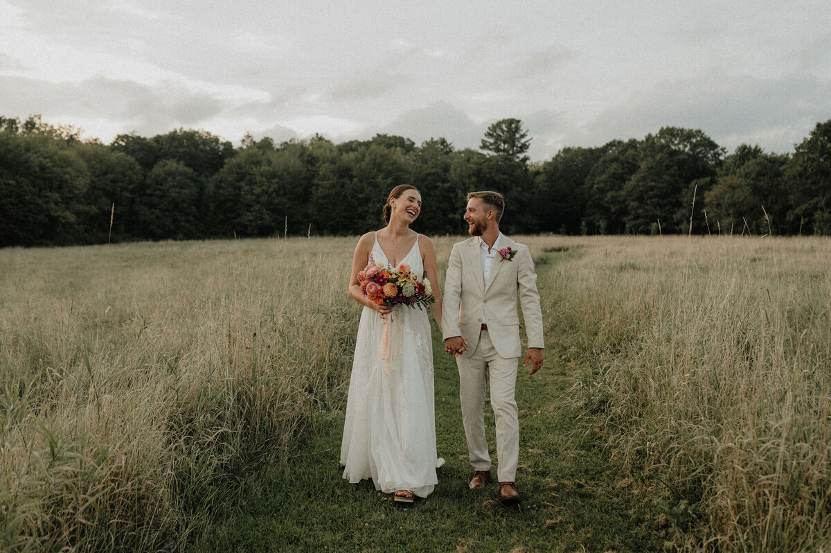 Maine couple walking in field holding hands with floral bouquet