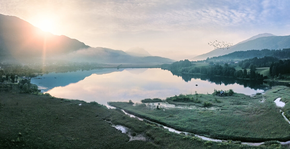Stimmungsvolle Morgenstimmung am Pressegger See mit Nebel, Sonnenaufgang und Vogelschwarm – professionelle Landschaftsfotografie vom Fotograf Atelier Schulte, spezialisiert auf Alpen- und Seenlandschaften in Kärnten.