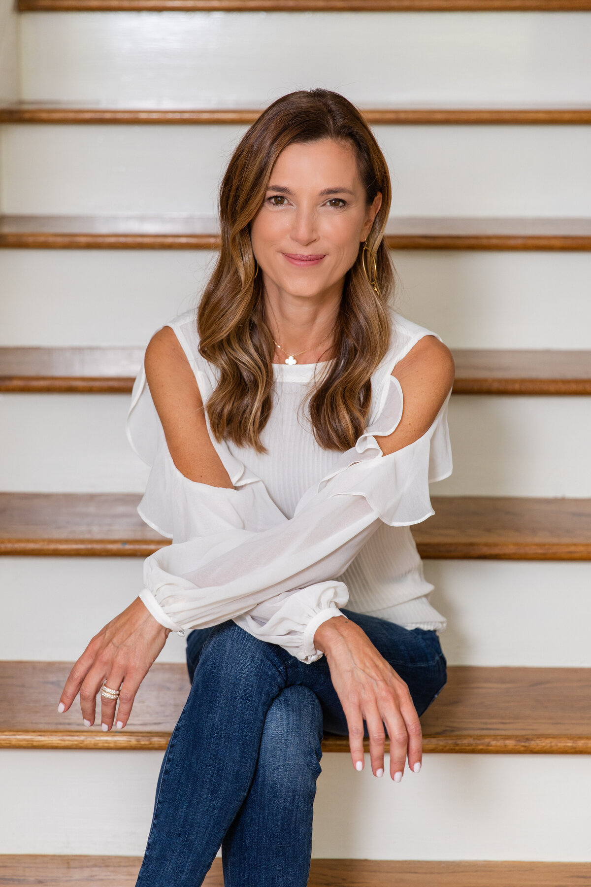 woman headshots in jeans and white top sitting legs crossed on stairs