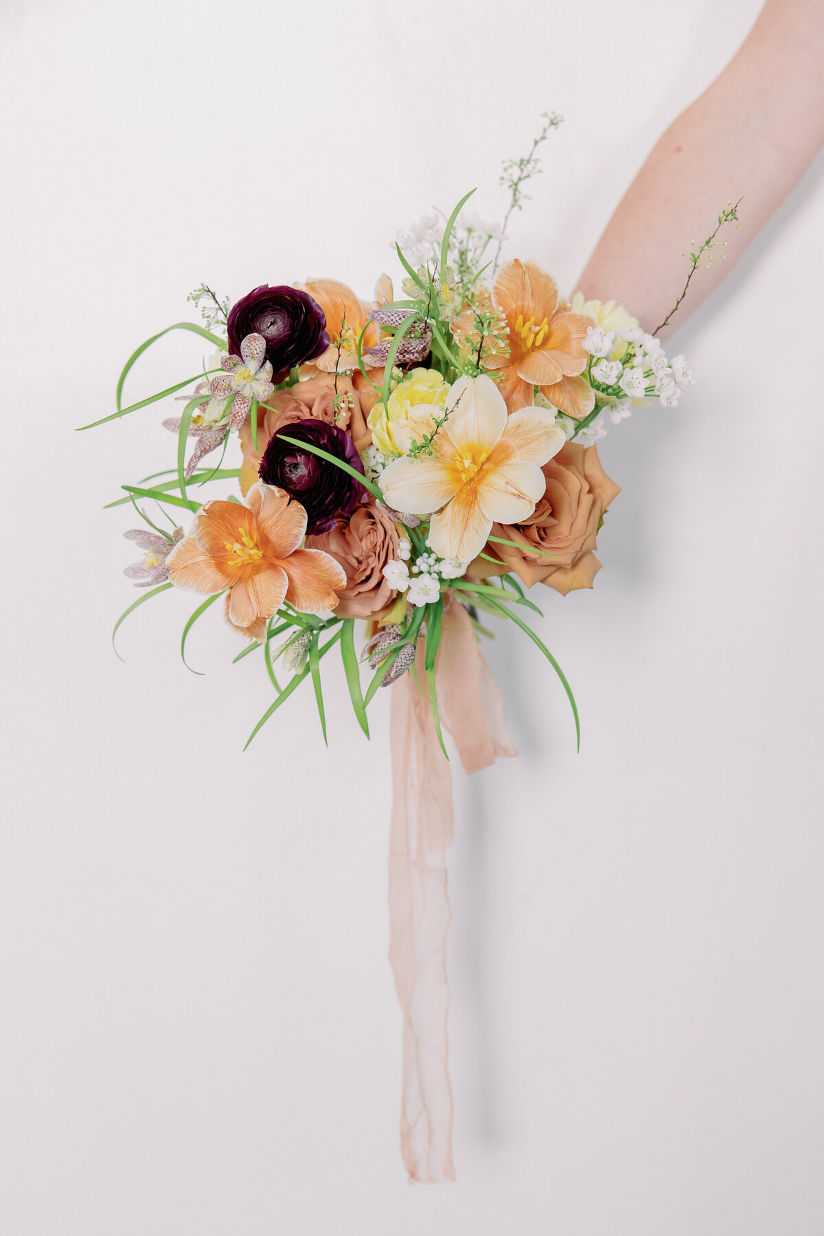 A person holds a bouquet with orange, white, and dark purple flowers.