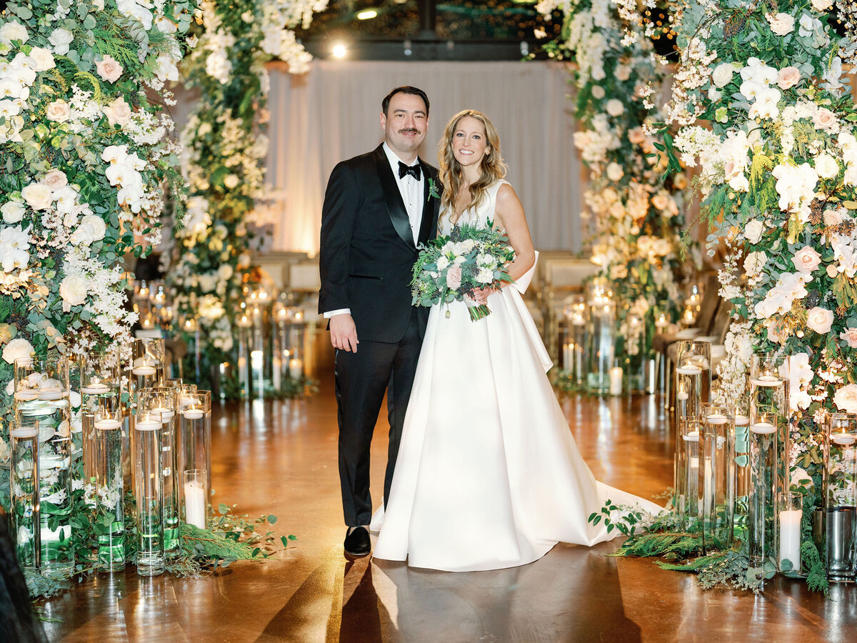 The bride and groom pose under a floral arch at the Theater on the Lake.