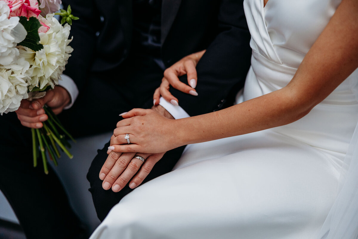 Close up of bride and groom holding hands while seated showcasing their wedding rings. Photo by Acacia & Grace Photography, a Canberra Wedding Photographer