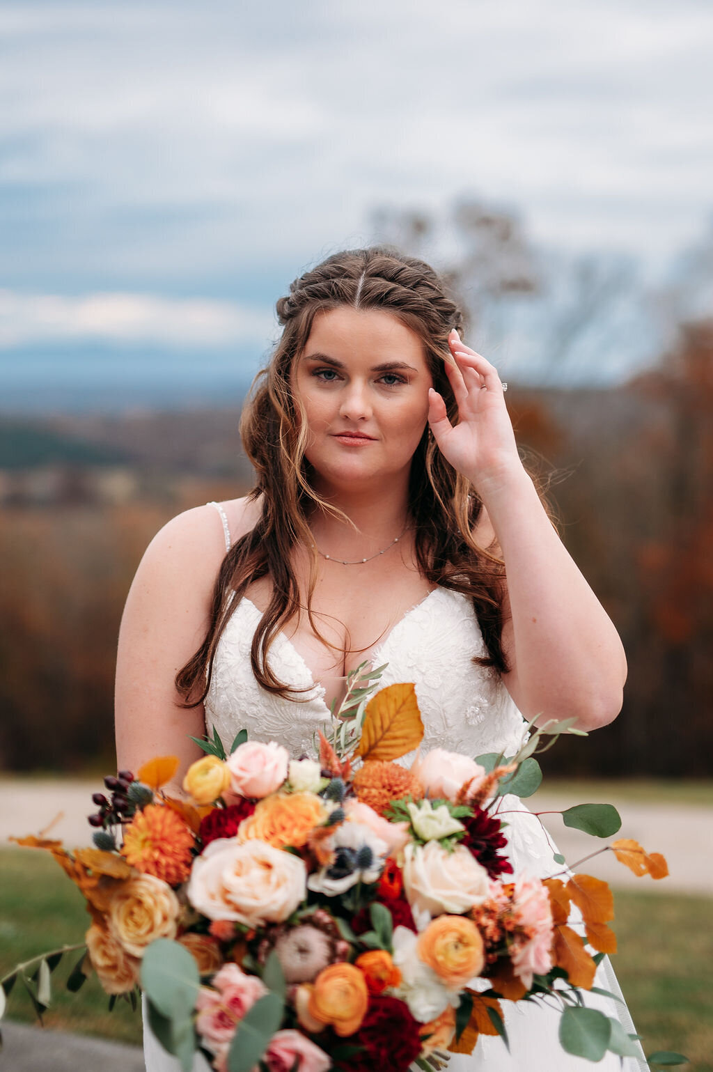 Bride holding a large fall colored bouquet while standing outdoors on a beautiful day
