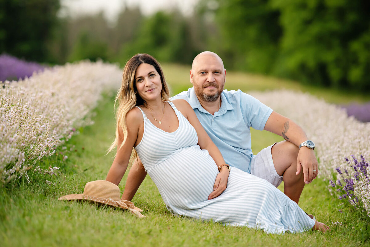 pregnant wife and husband sitting in a lavender field for her summer outdoor fall maternity photos in Burlington