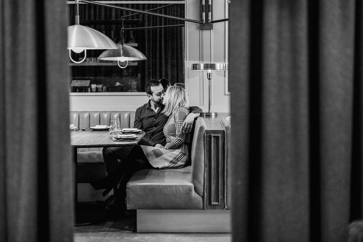 A black and white engagement photo of a couple kissing in a West Loop restaurant booth