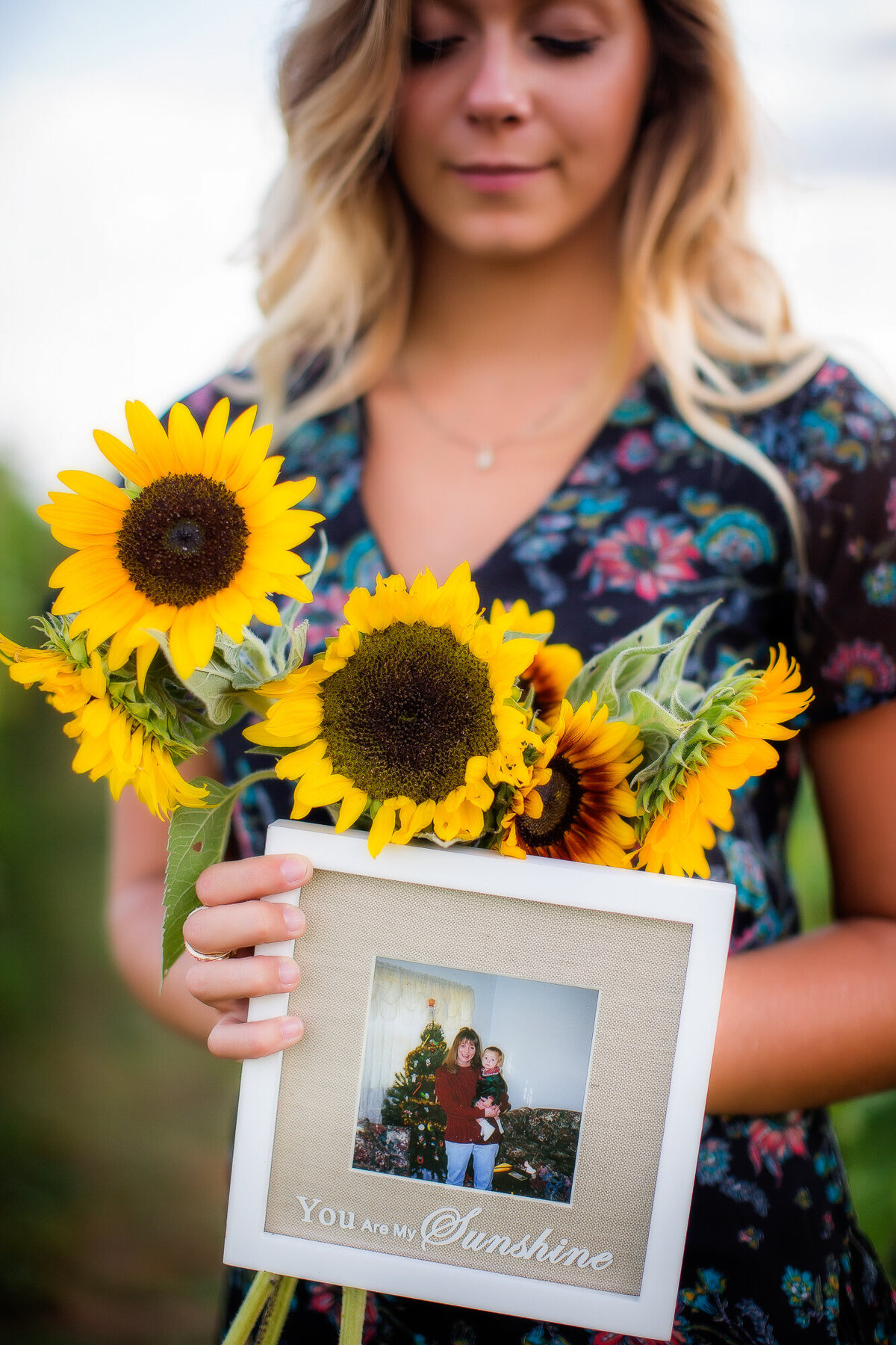 Senior girl holding sunflowers and an image of herself with her mom that passed when she was young