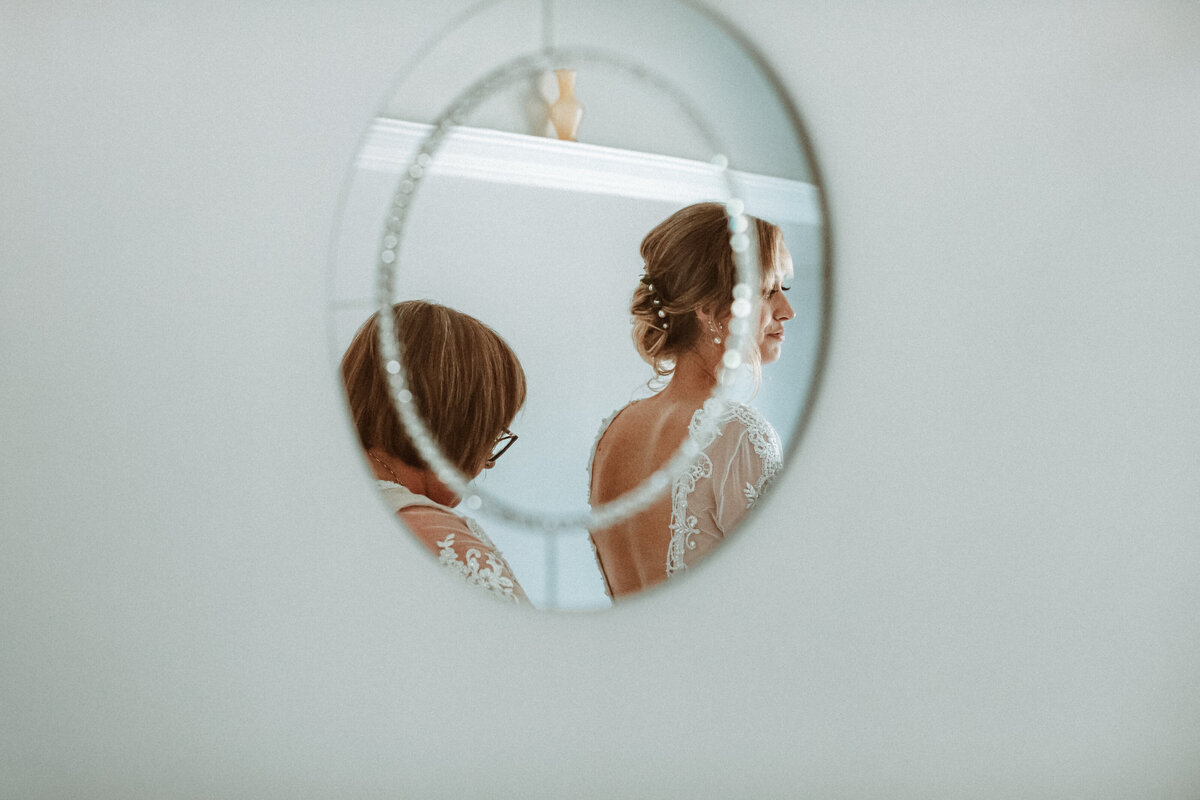 reflection of a mother dressing the bride in a round mirror