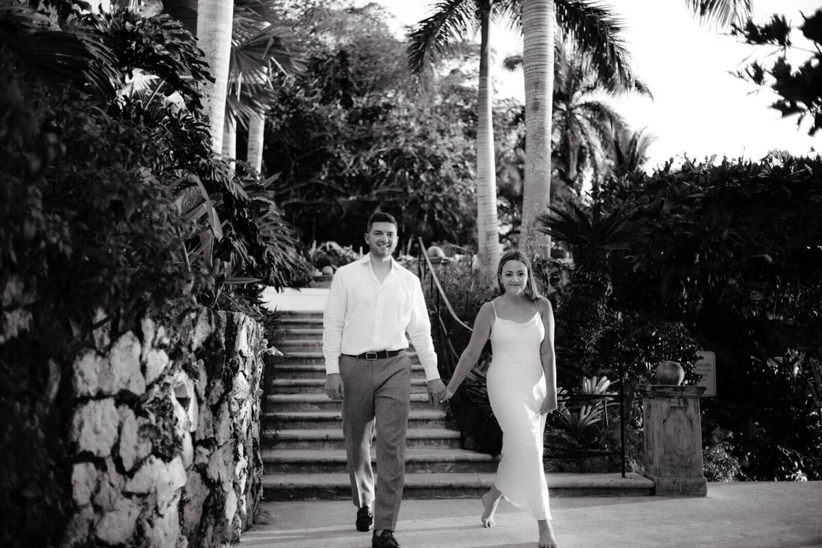 Black and white photo of the engaged couple walking outdoors at Round Hill Hotel & Villas, Jamaica.