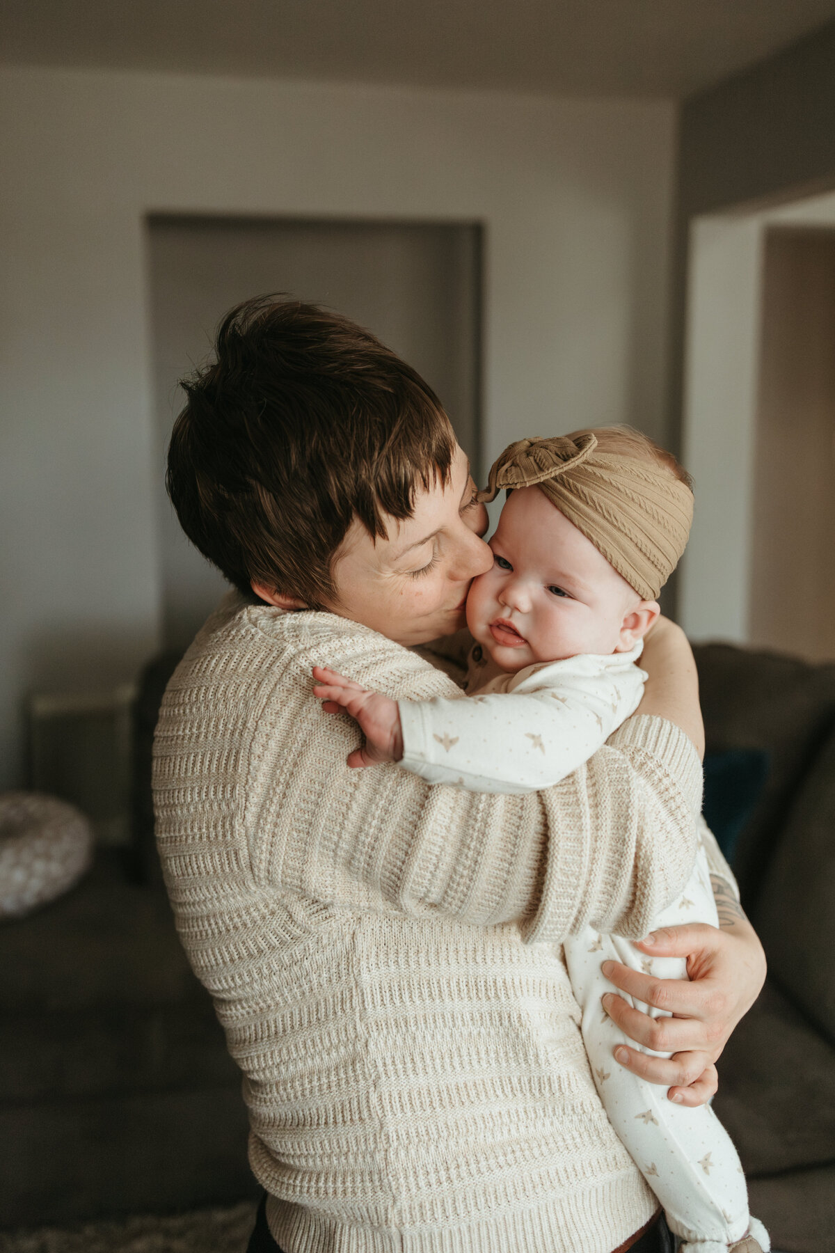 mom kissing baby girl with tan bow on the cheek during in home family session in longmont colorado