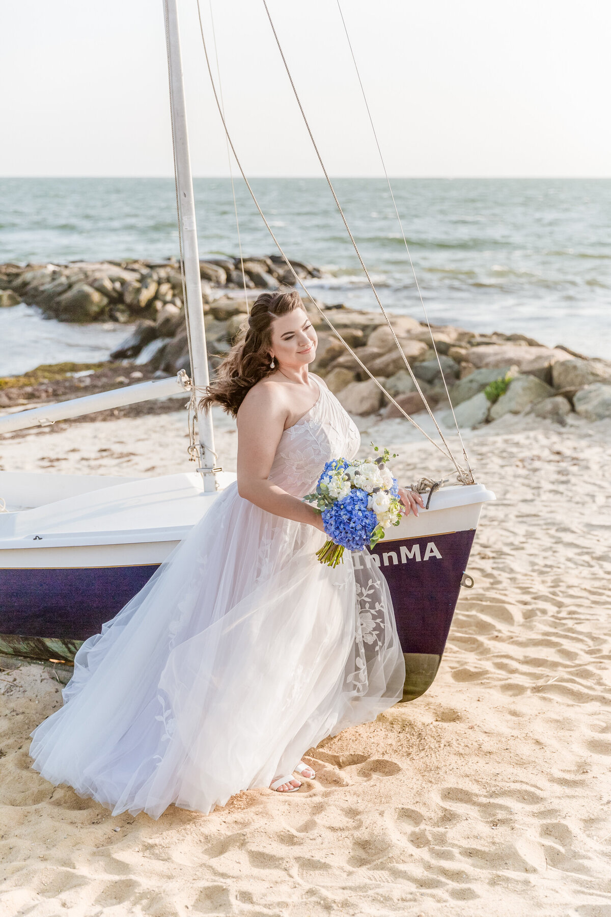 A bride stands near a sail boat for her costal wedding on Cape Cod