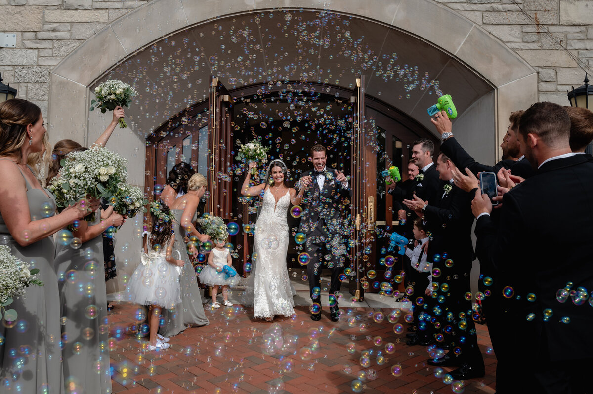 Bride and groom exit church surrounded by bubbles