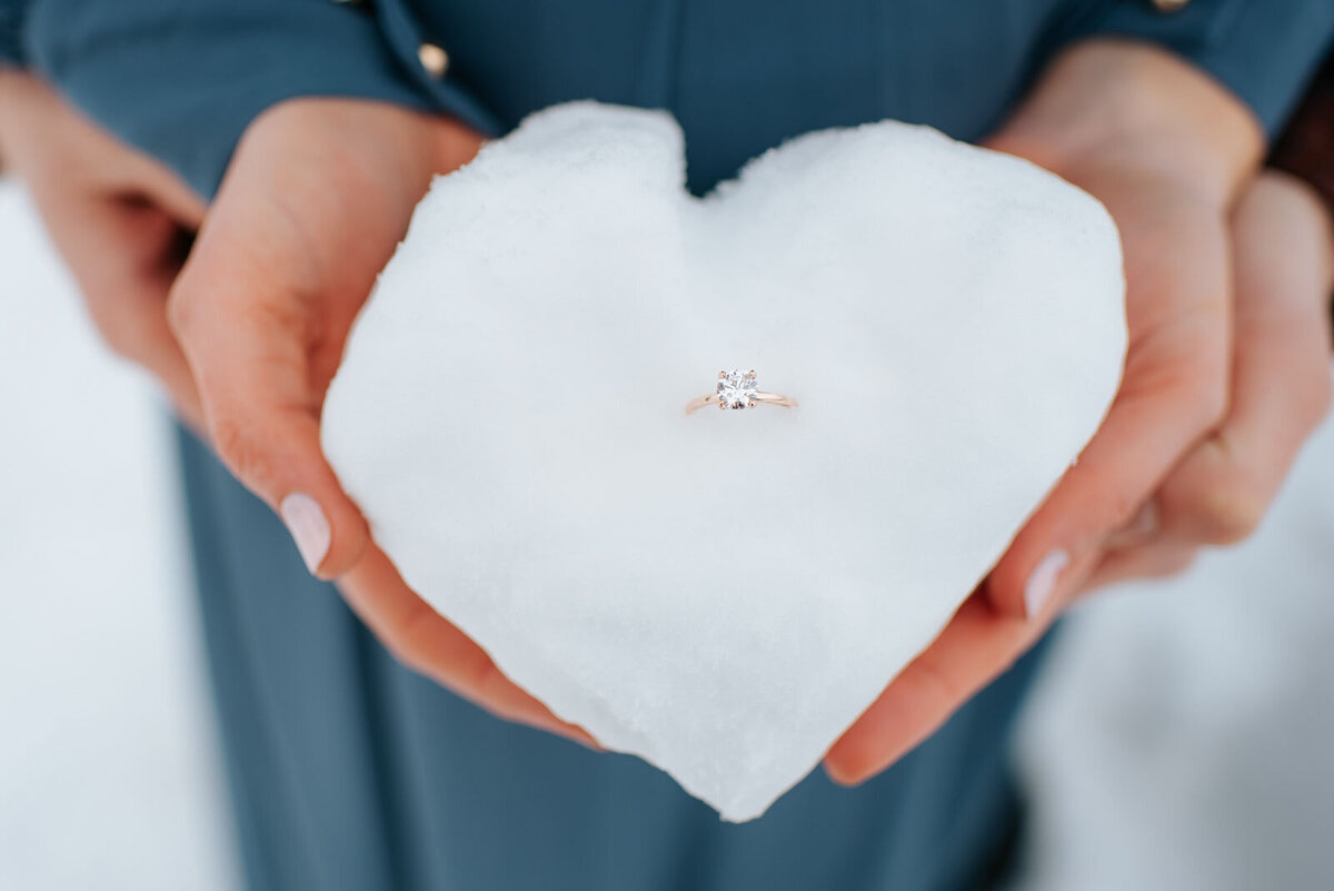 couple holding engagement ring in snowball at killington mountain