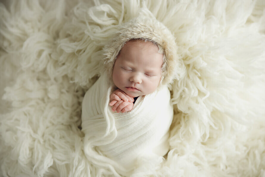 Baby wrapped in off-white and an eskimo hat sleeps during her studio photo session.