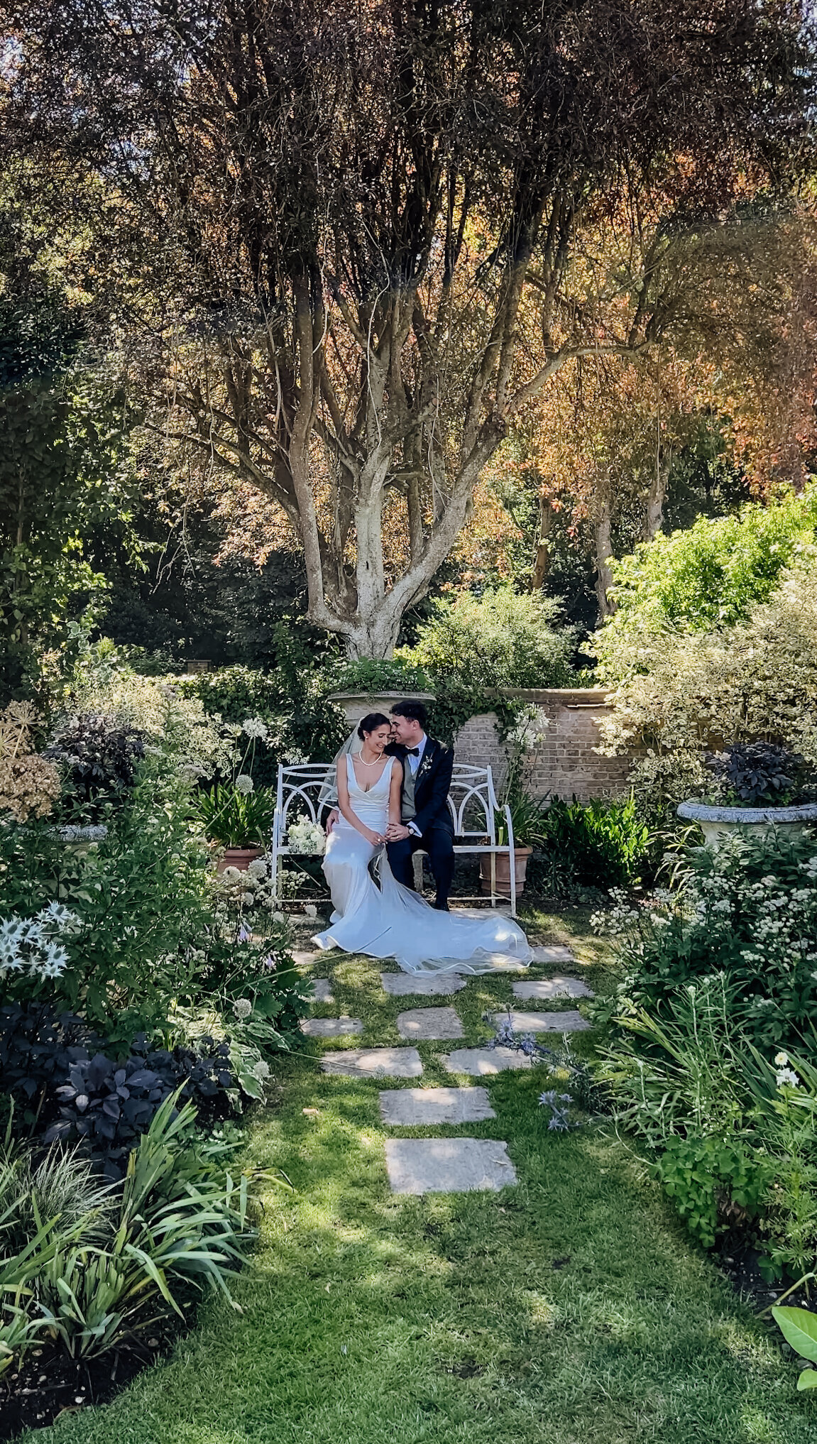 Couple sitting on bench having a quiet moment in lush gardens during wedding reception captured by Suffolk Wedding Content Creator
