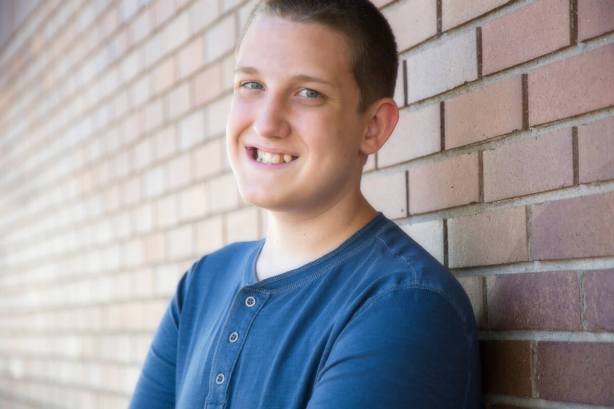 Young man smiling in front of a brick wall and wearing a blue shirt