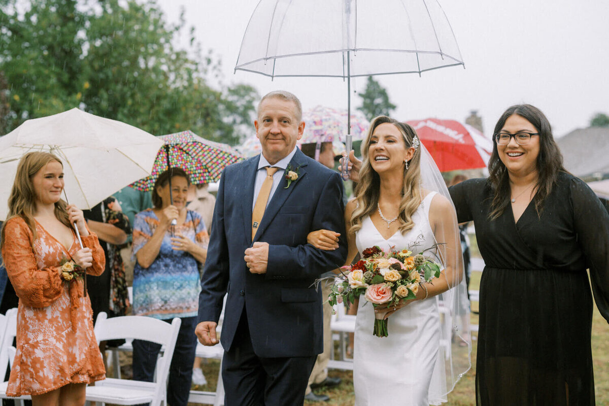 bride-and-dad-walk-under-umbrella-in-the-rain
