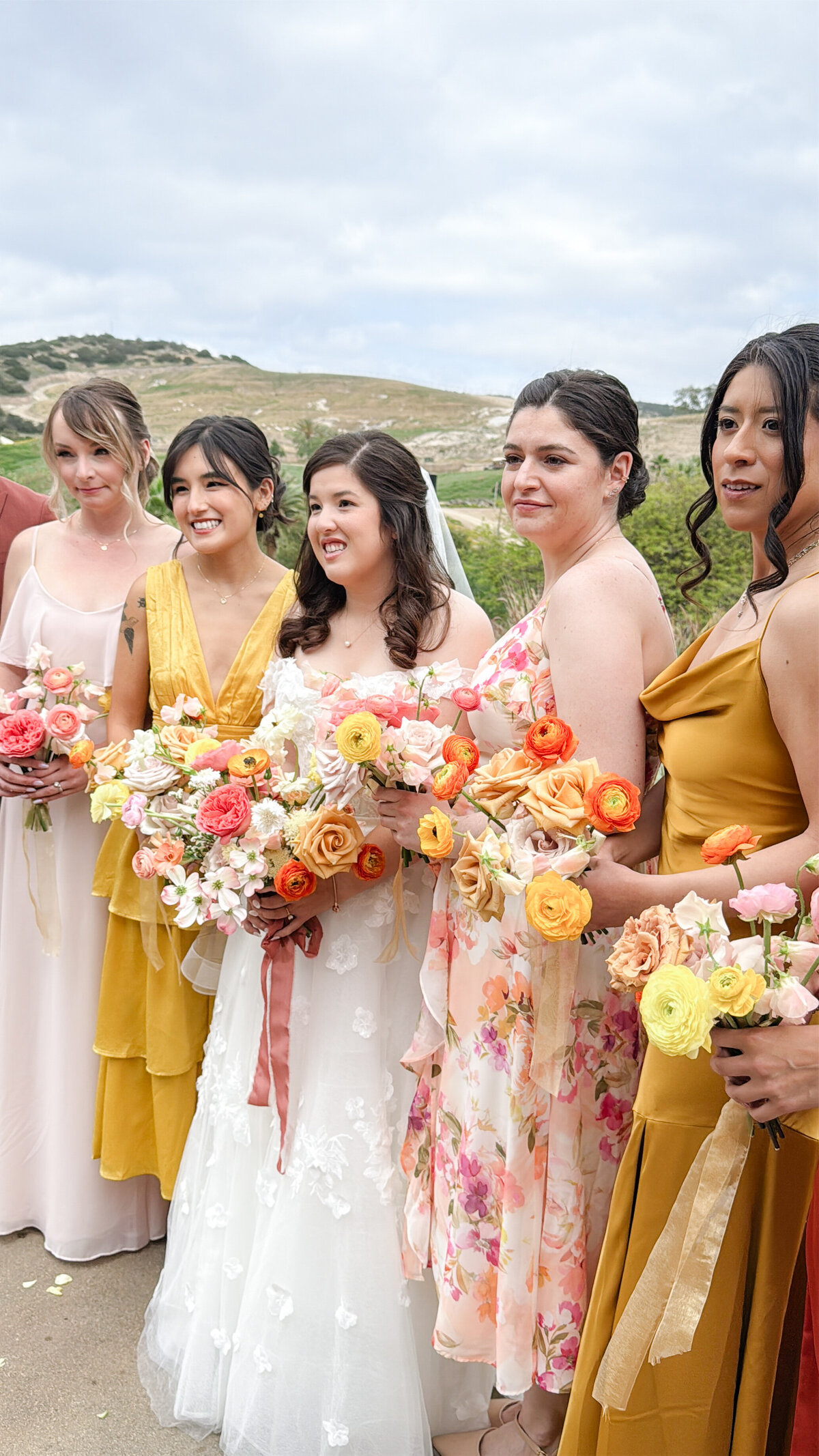 Bride smiling with her bridal party in colorful bridesmaids dresses with pink, orange and yellow bouquets at the San Diego Safari Park.