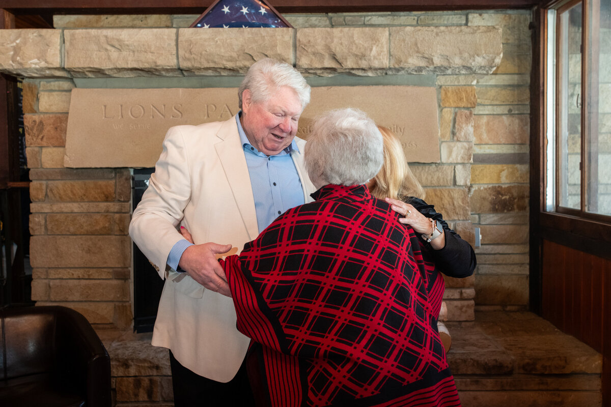 man welcomes guest in front of a fireplace