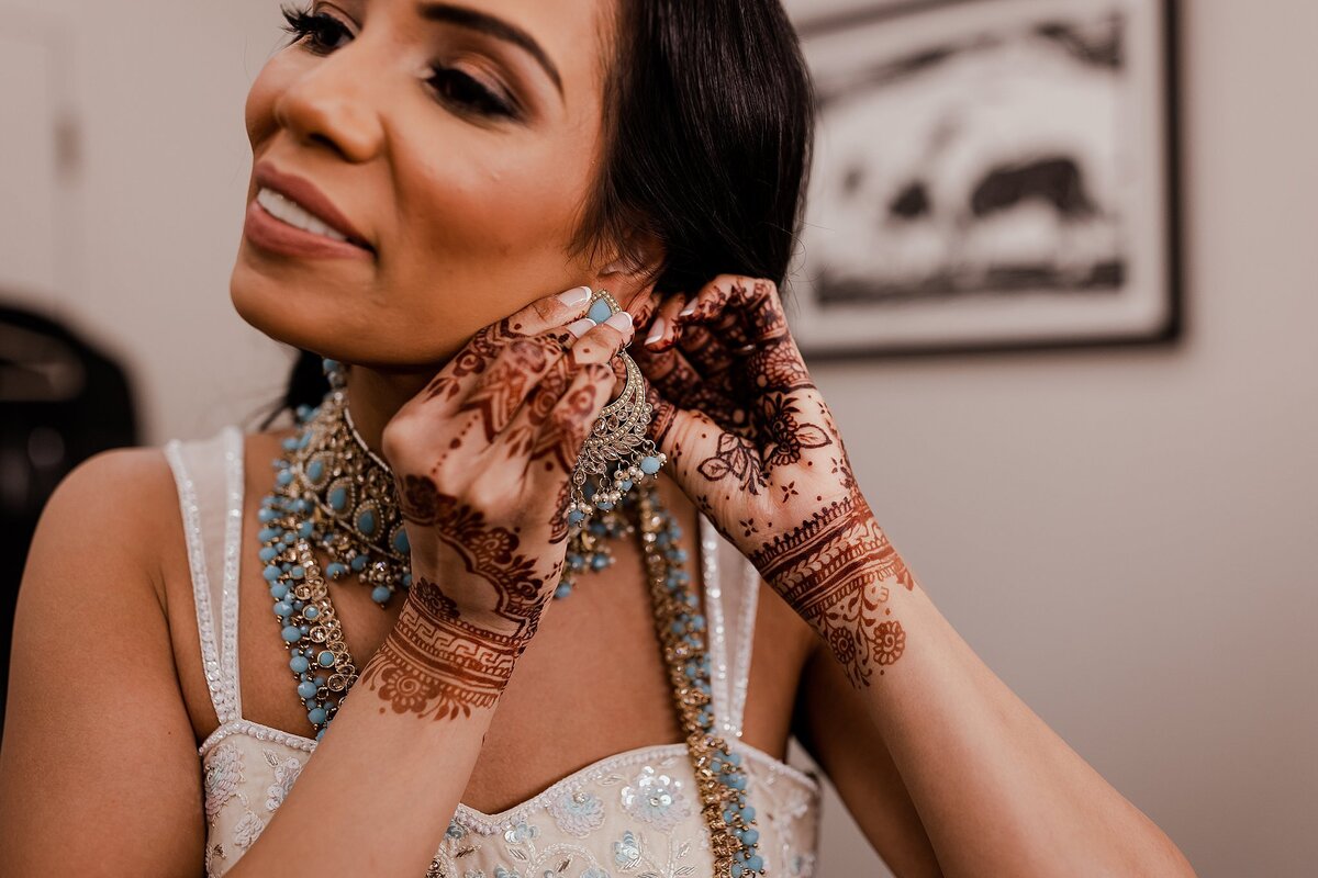 Hindu bride puts on her light blue and gold Indian wedding jewelry for her Nashville wedding. The Hindu bride shows off the wedding henna from her mendhi on her hands.